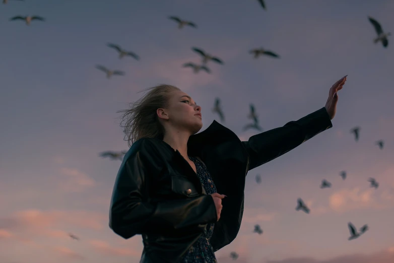 a woman stands looking up as the birds fly behind her