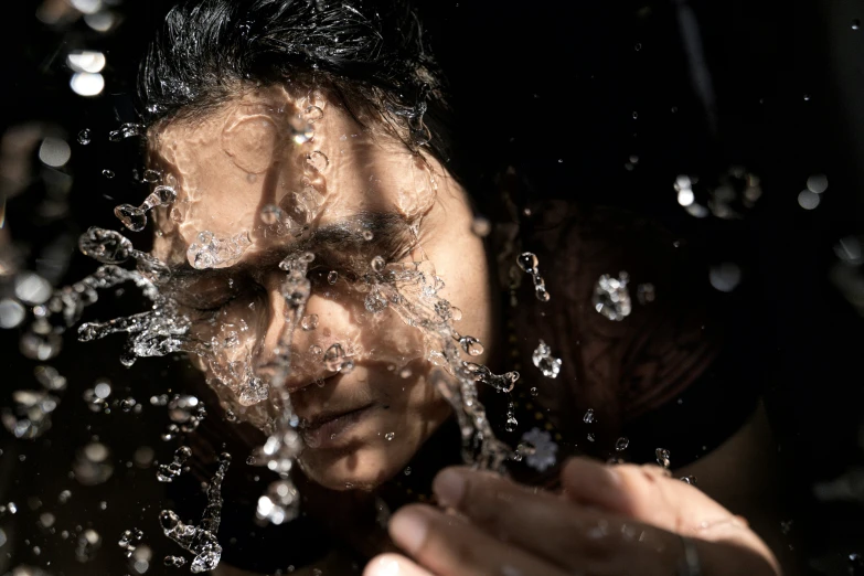 water spilling on a young man who is holding his hand over his face