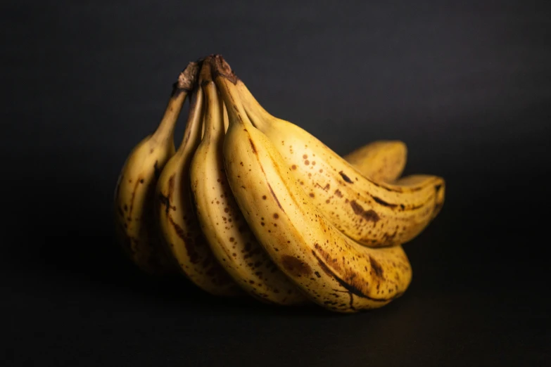 several ripe bananas on a dark surface, one bunch has small brown spots
