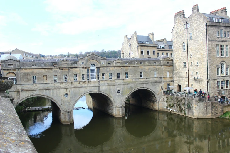 an old bridge is spanning over some water in front of older buildings