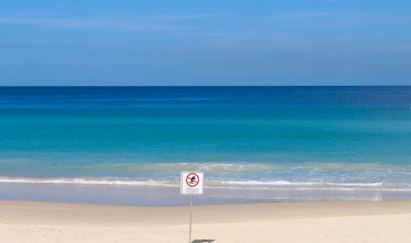 a red and white sign on the sand next to a beach