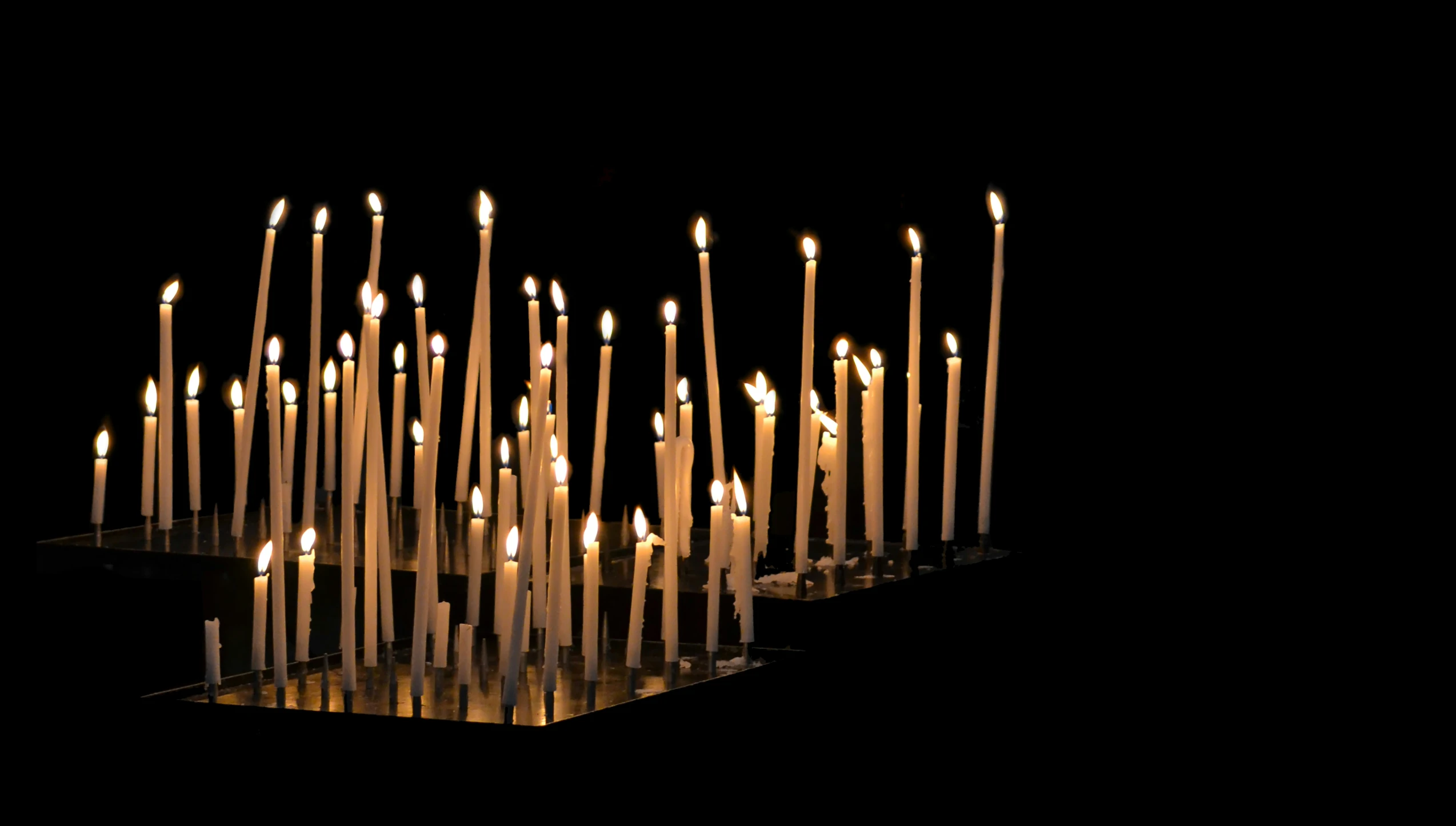 several rows of candles are glowing in the dark