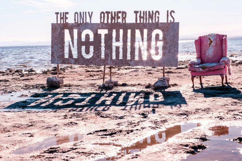 a sign is sitting in the sand beside a chair