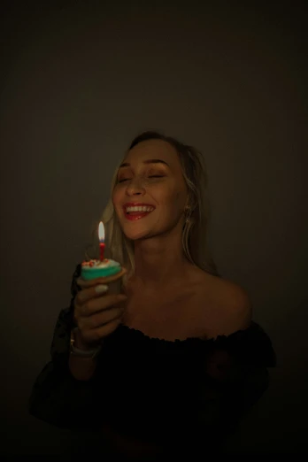 the woman holds a small lit candle while she has her face close to her mouth