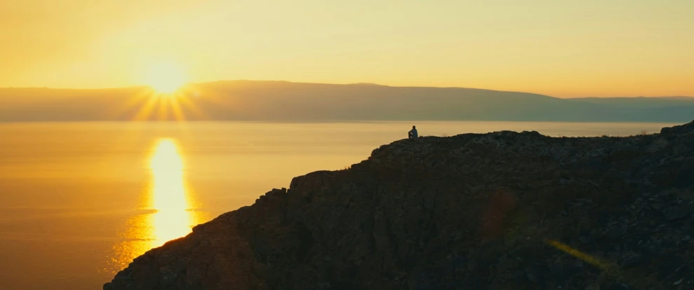 man standing on a hill overlooking the ocean at sunset