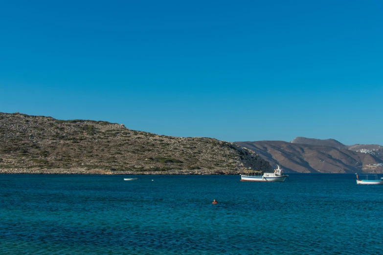 two boats are anchored near a mountainous shore