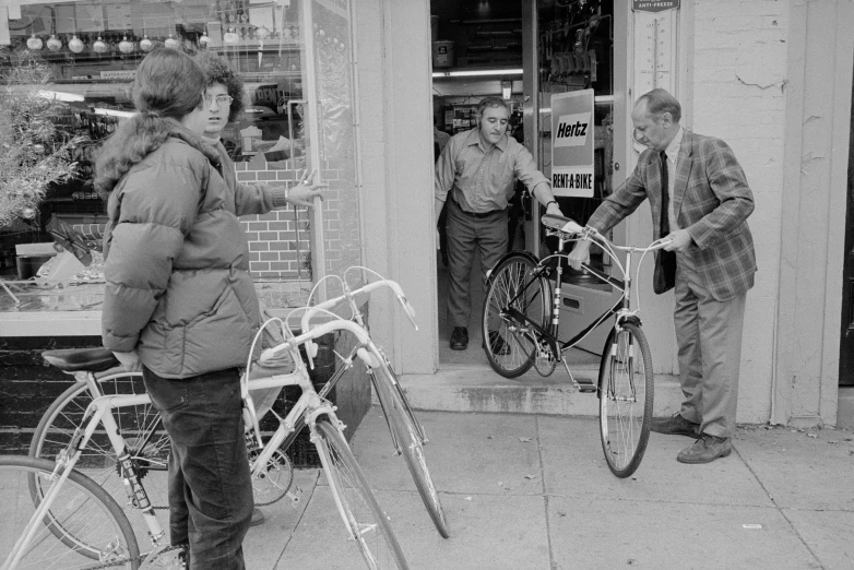 two people holding bicycles while standing on the sidewalk