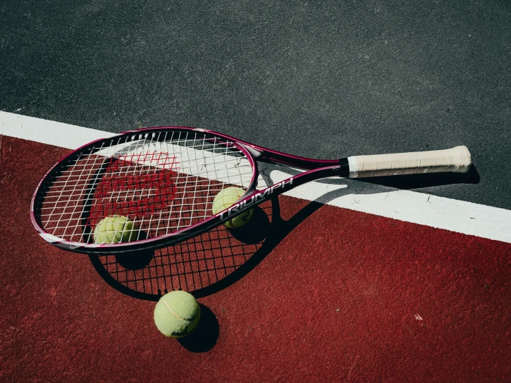 a red tennis court with a racquet and three tennis balls