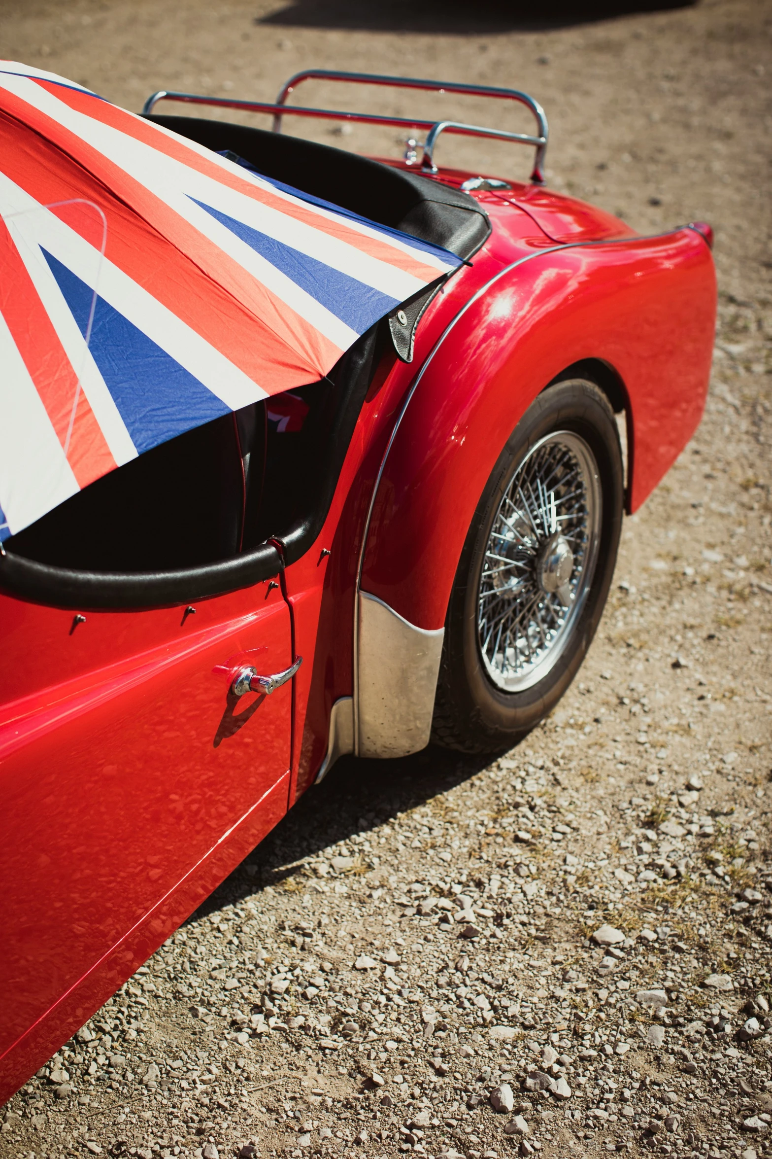 an open british style red sports car with a big umbrella on the roof