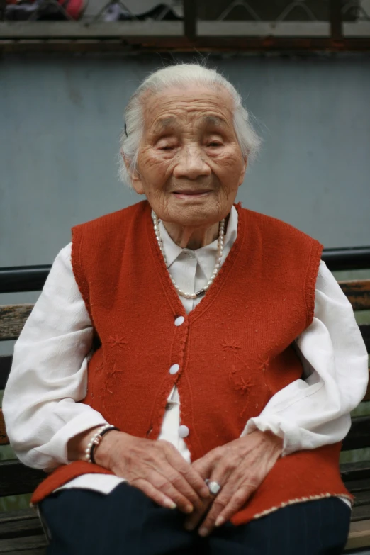 an elderly woman sitting on a park bench wearing a red vest