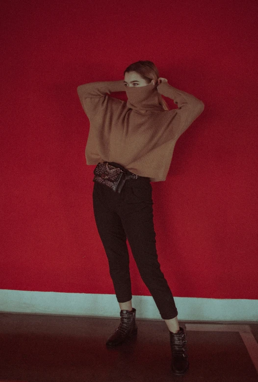 woman leaning against red wall wearing black pants