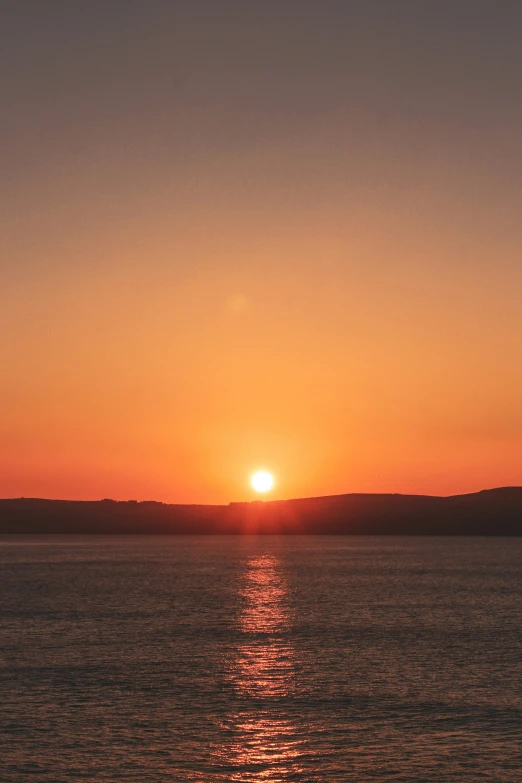 the sun is setting over water off a beach