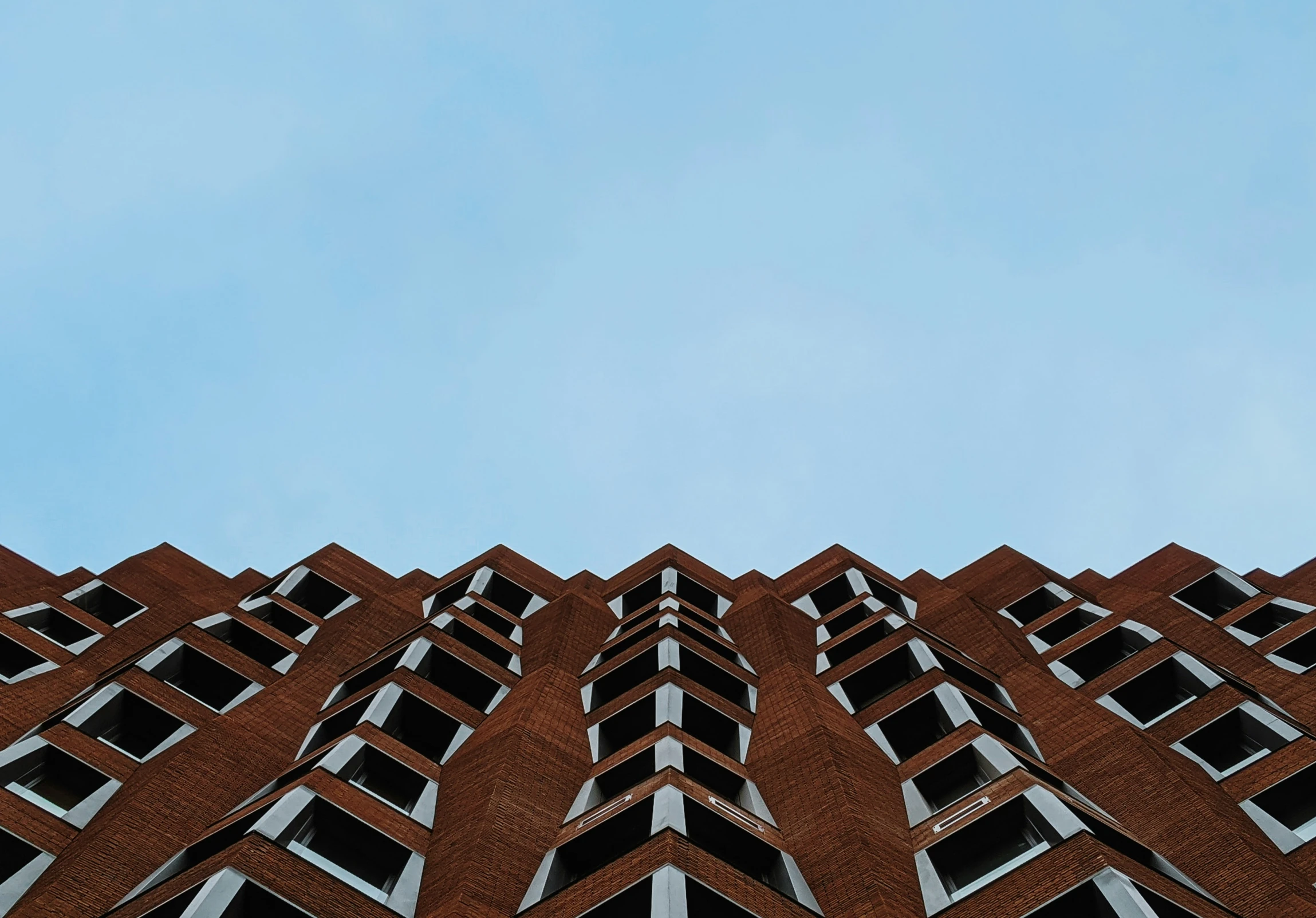 the face of a brick building with balconies and windows against a blue sky