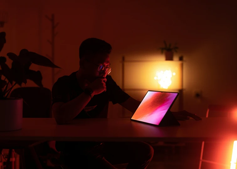 a person sitting at a desk in the dark on their laptop computer