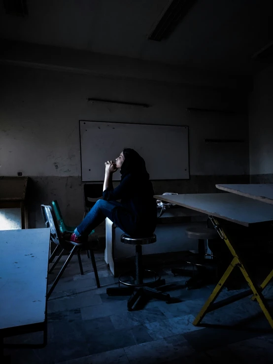 a dark room with two tables, a laptop and a person seated in the middle of it