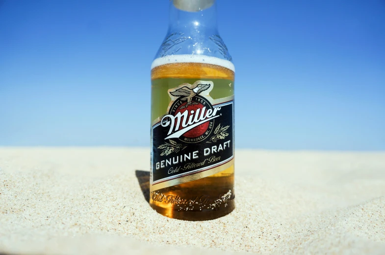 an empty bottle of beer sits on the sand