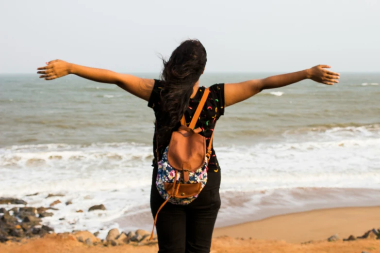 a woman standing in front of the ocean with her arms spread out