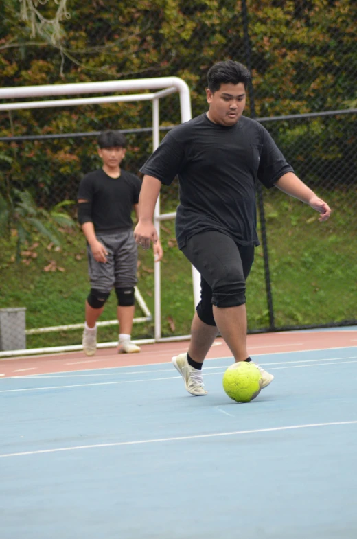 two young men playing with a yellow ball on a blue tennis court