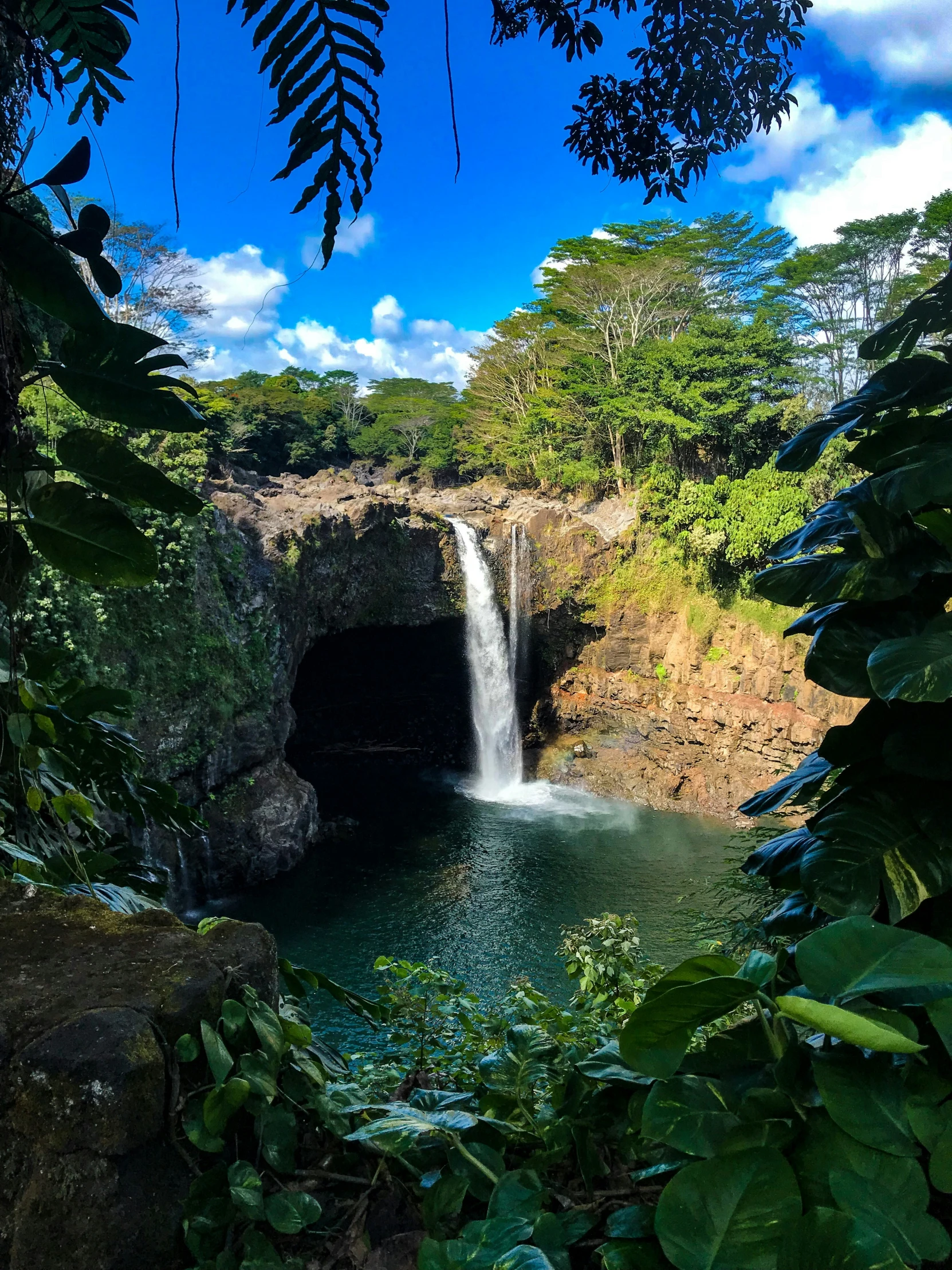 water falls coming out from a deep cave into a large pool