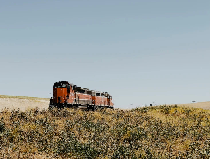 an orange train is coming down the tracks on the hillside