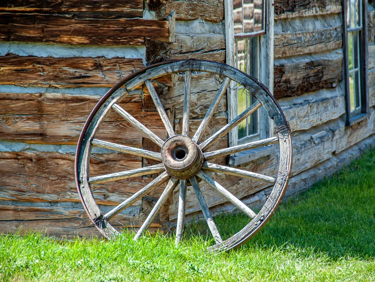 an old wooden wagon wheel is in front of a house