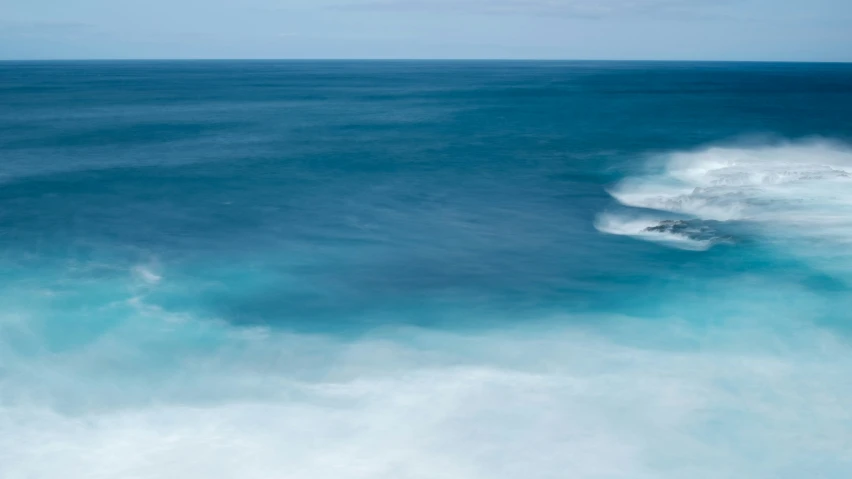 a white water wave in an ocean with blue sky