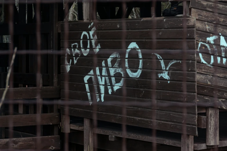 some writing on a wooden box behind a chain link fence