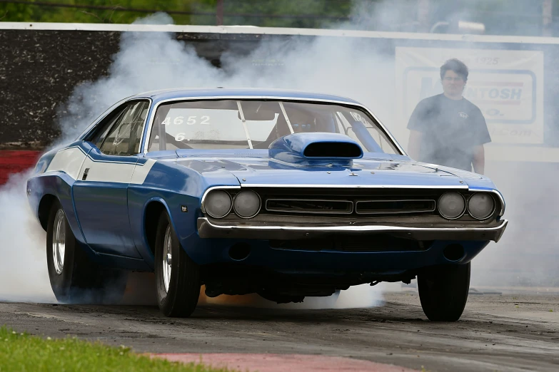 a blue muscle car drives on a track with smoke coming from it