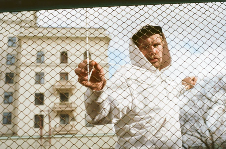 a man is holding up a lighter outside behind a metal fence