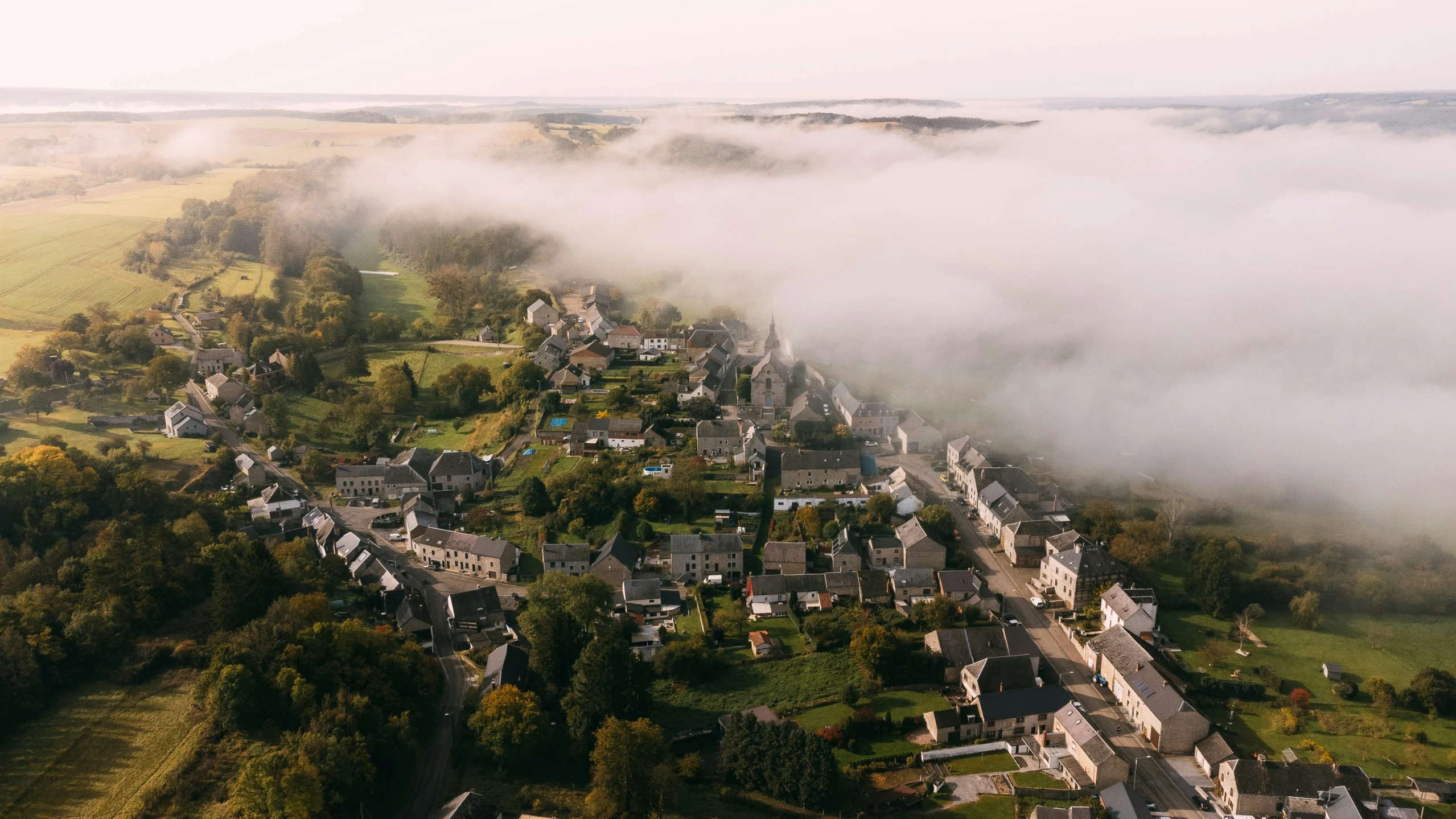 fog hovering above a small village that sits in the middle of an open field