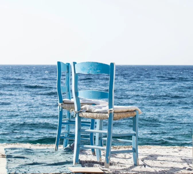 two blue chairs on the beach by some water