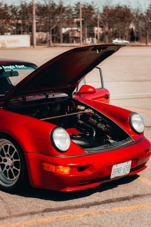 a red porsche parked in a parking lot with the hood up
