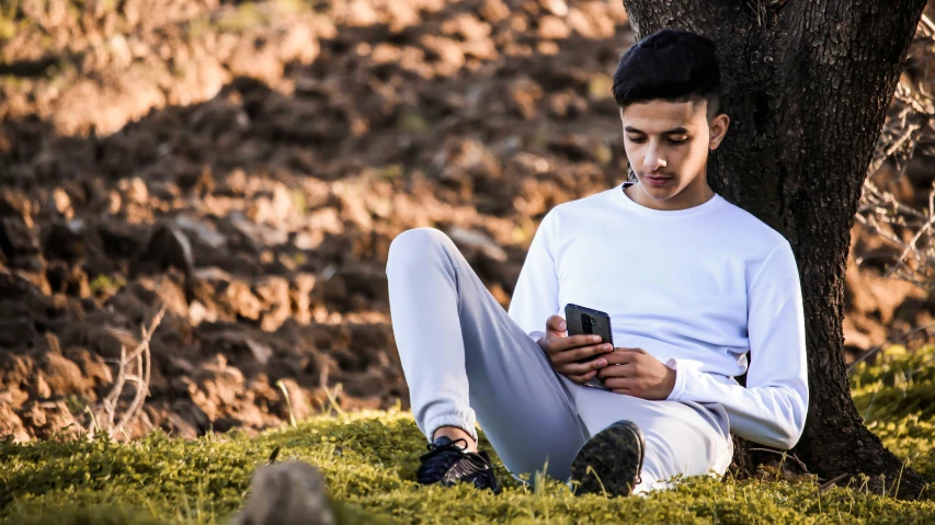 a man sitting next to a tree with a cellphone