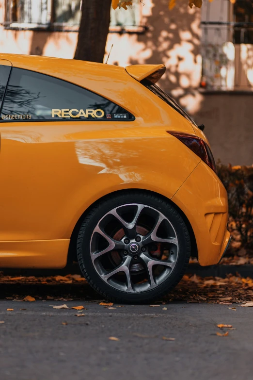 a orange car parked by a tree with leaves on the ground