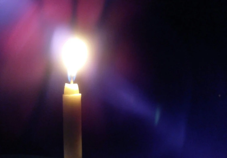 a lit candle in the dark of night with blurry light on the candle