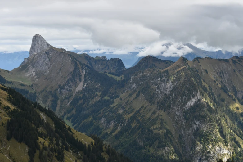 view from high up on several rocky mountain peaks with green valleys under the clouds