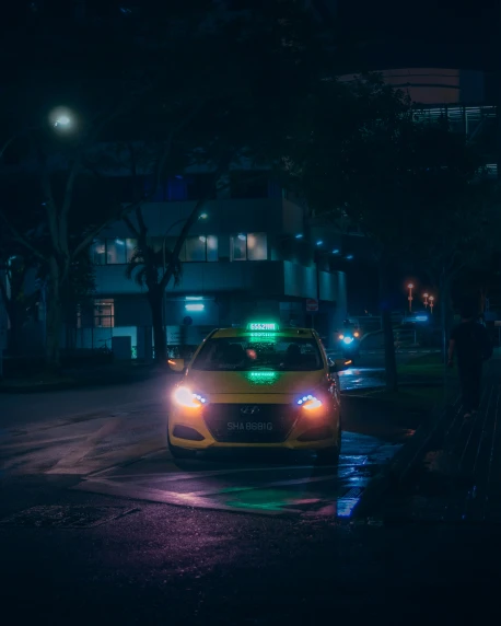 a yellow car with its lights on driving down a road at night