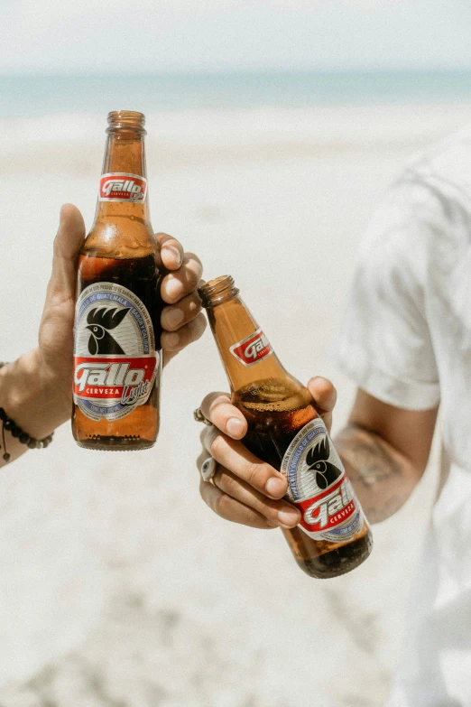 two people on the beach holding up two beers