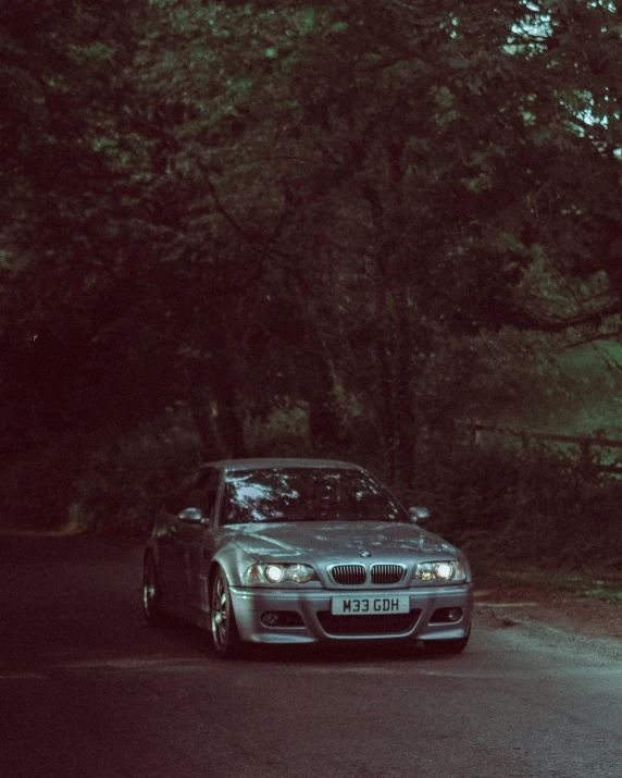 a silver bmw parked in front of trees on the side of the road