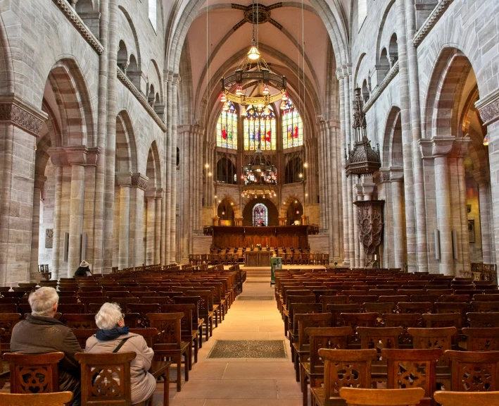 two people sitting in pews facing toward the side of a large church