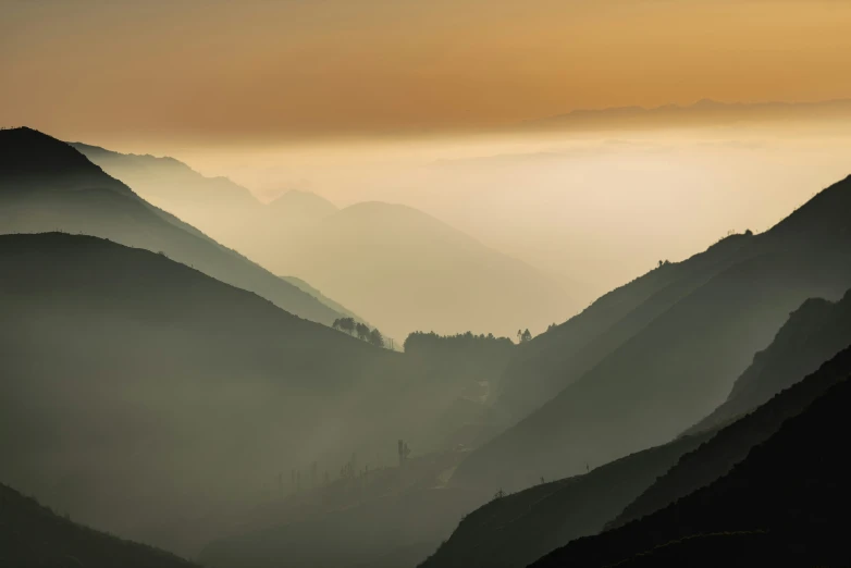 the sun rises over the mountains with a few trees on top