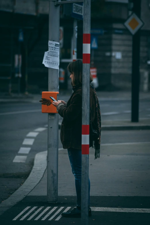 a woman stands next to a street sign, looking at her cell phone