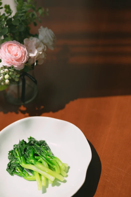 a plate with vegetables and some roses in a vase behind it