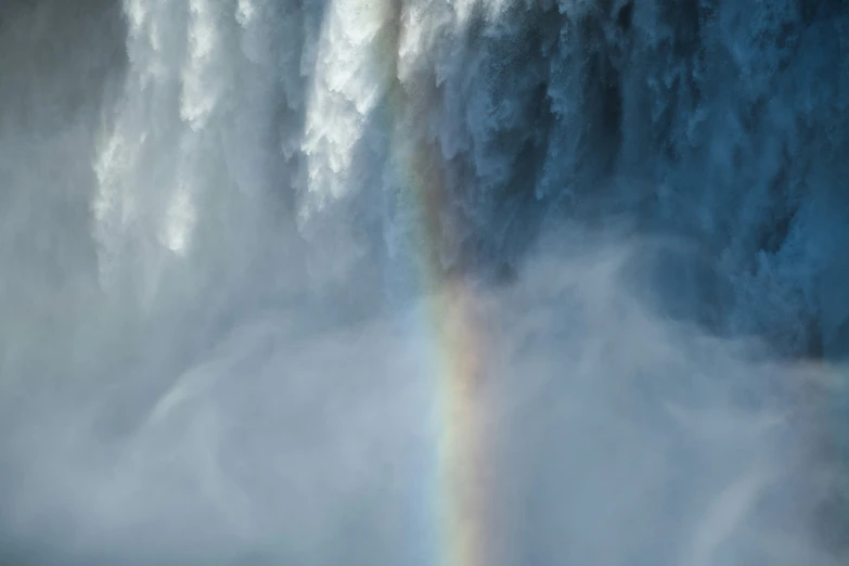 rainbow visible from behind a massive wave with a man looking out the ocean