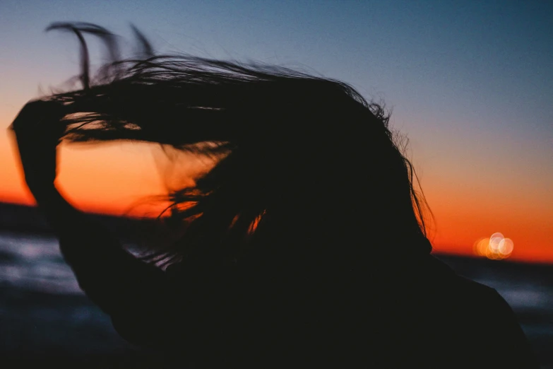 a girl holds her hair back in front of the sunset