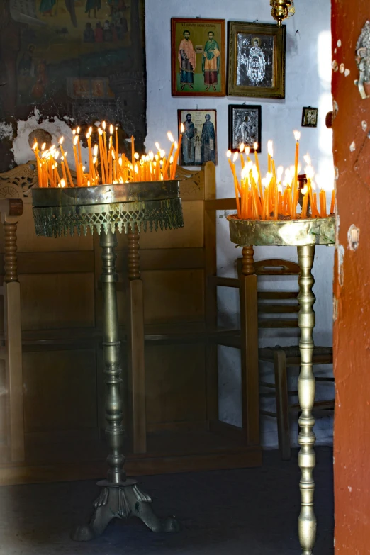 several lit candles sit on ornate stands in front of a wall