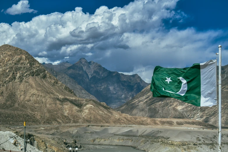 an pakistan flag flying in the wind in front of a mountain range