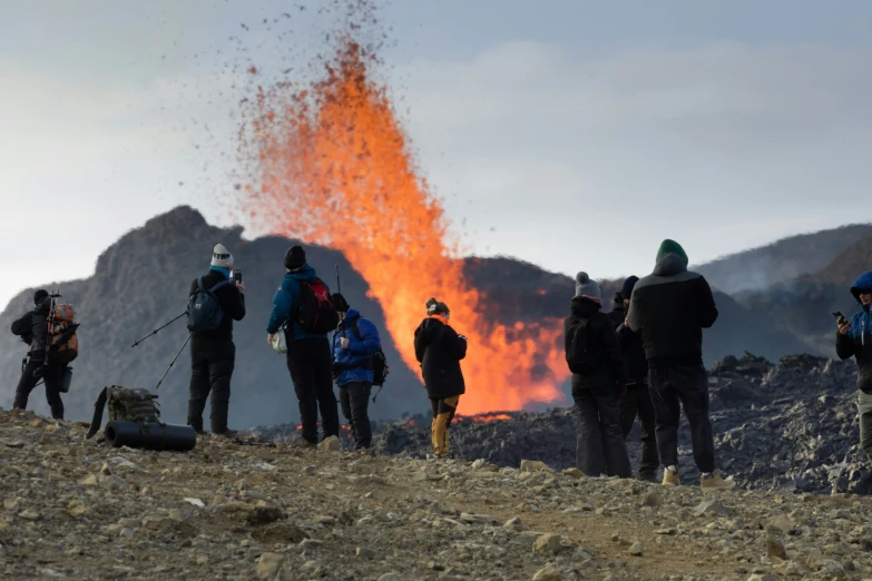 people standing at the top of a hill watching a huge plume of orange smoke