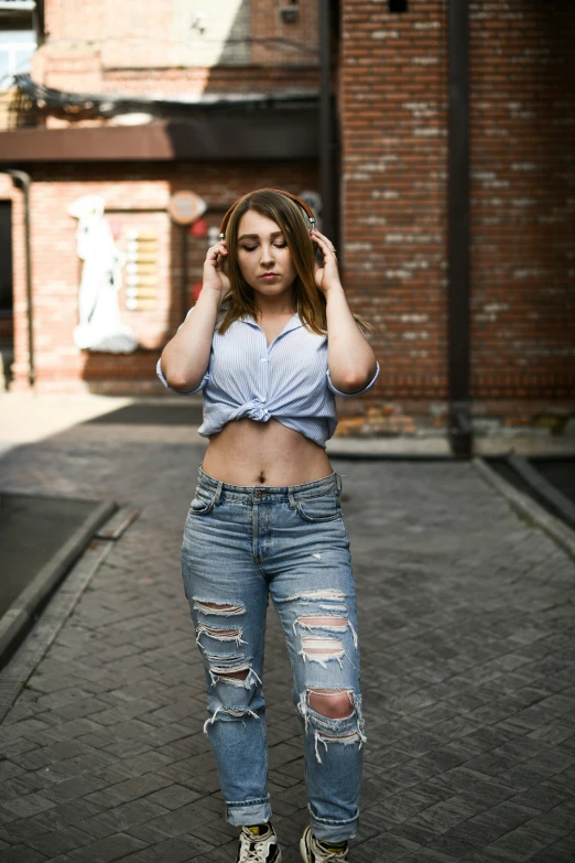 a woman stands outside in torn jeans and a gray shirt