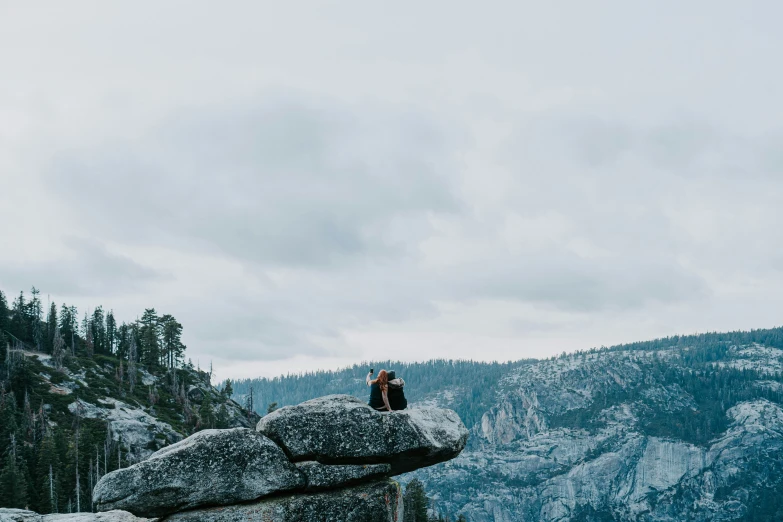 a person sitting on top of a large boulder near a mountain